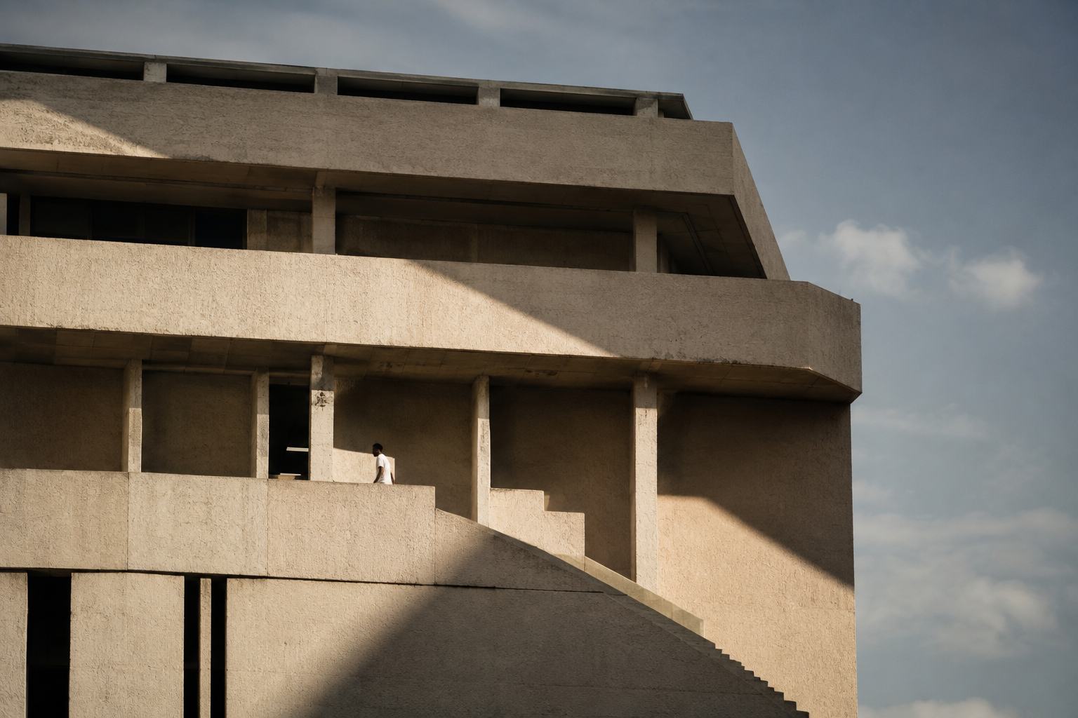 Modernist concrete building in raking light with a single figure on the stair.